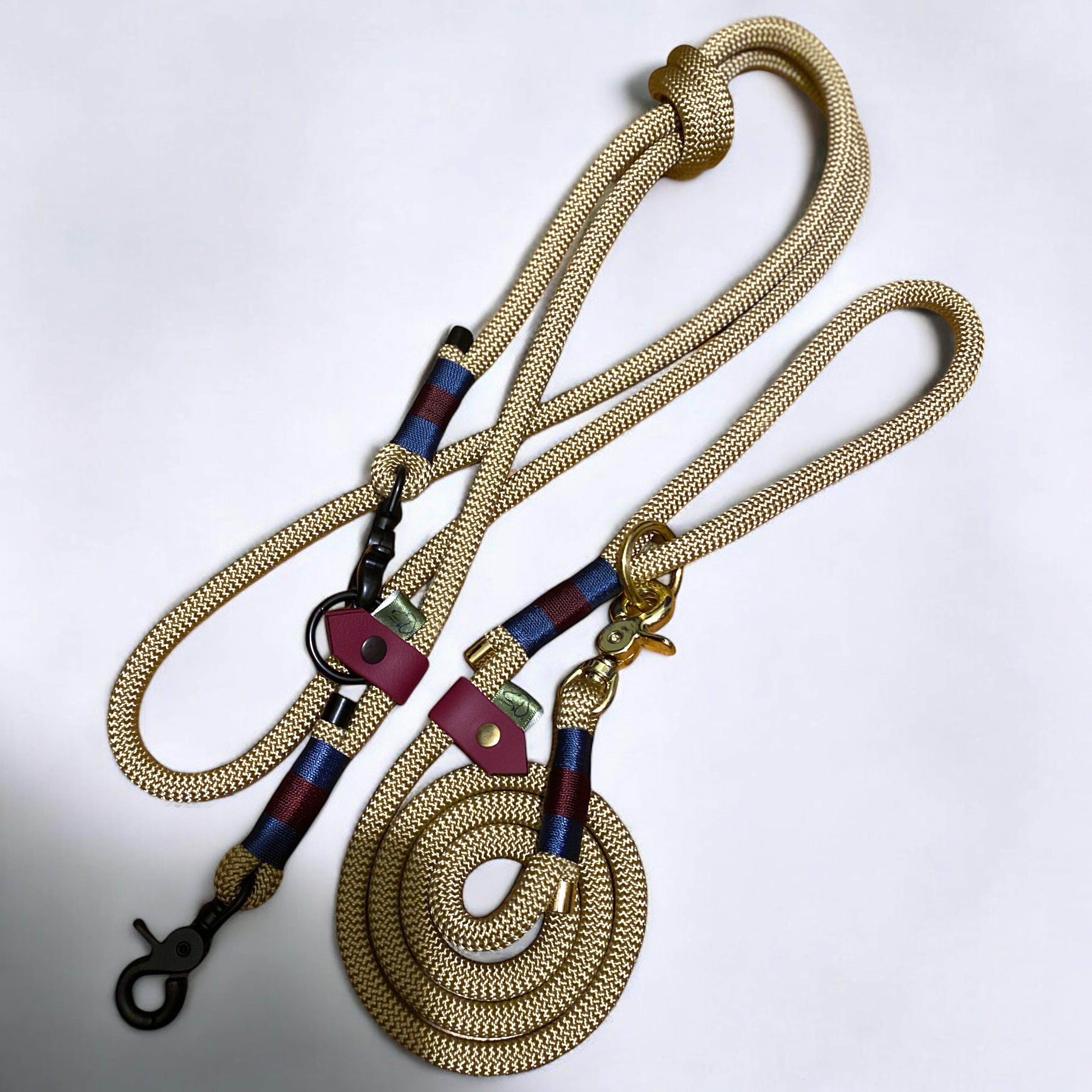 Two Green Dog leads in gold nylon rope with navy blue and maroon Greenwich Yarn binding. One is a regular lead with gold hardware, and the other is a handsfree adjustable lead with black hardware.