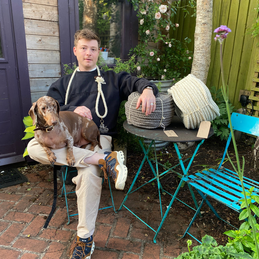 Person sitting outdoors with a his dog, surrounded by plants and wool.