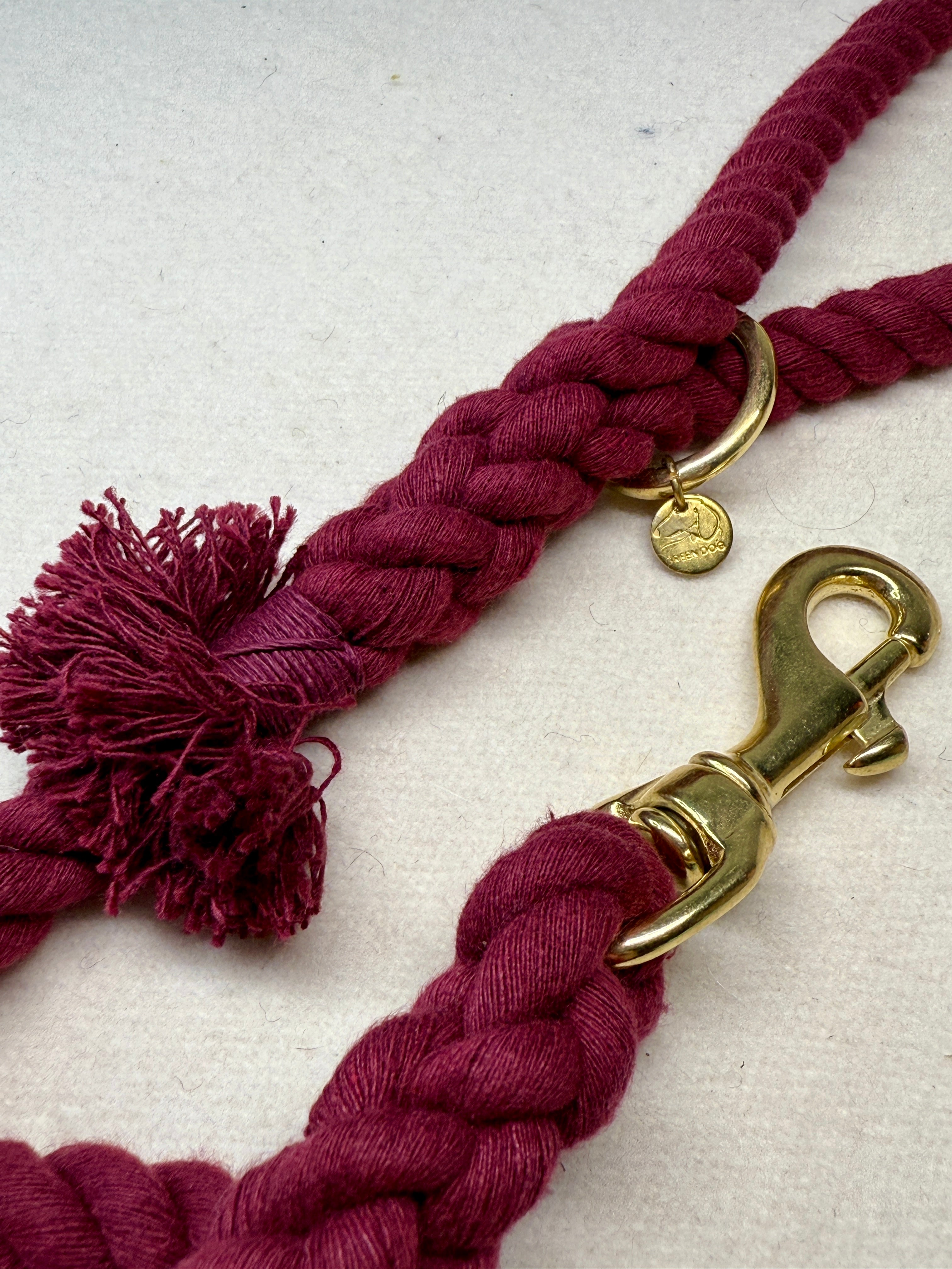 Close-up of the burgundy braided cotton rope dog lead with a brass clasp on a light woollen background