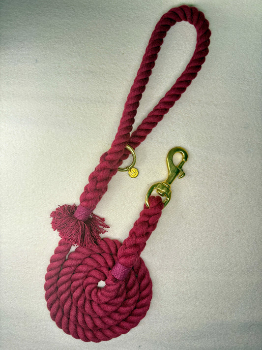 Burgundy braided cotton rope dog lead with a brass clasp on a light woollen background