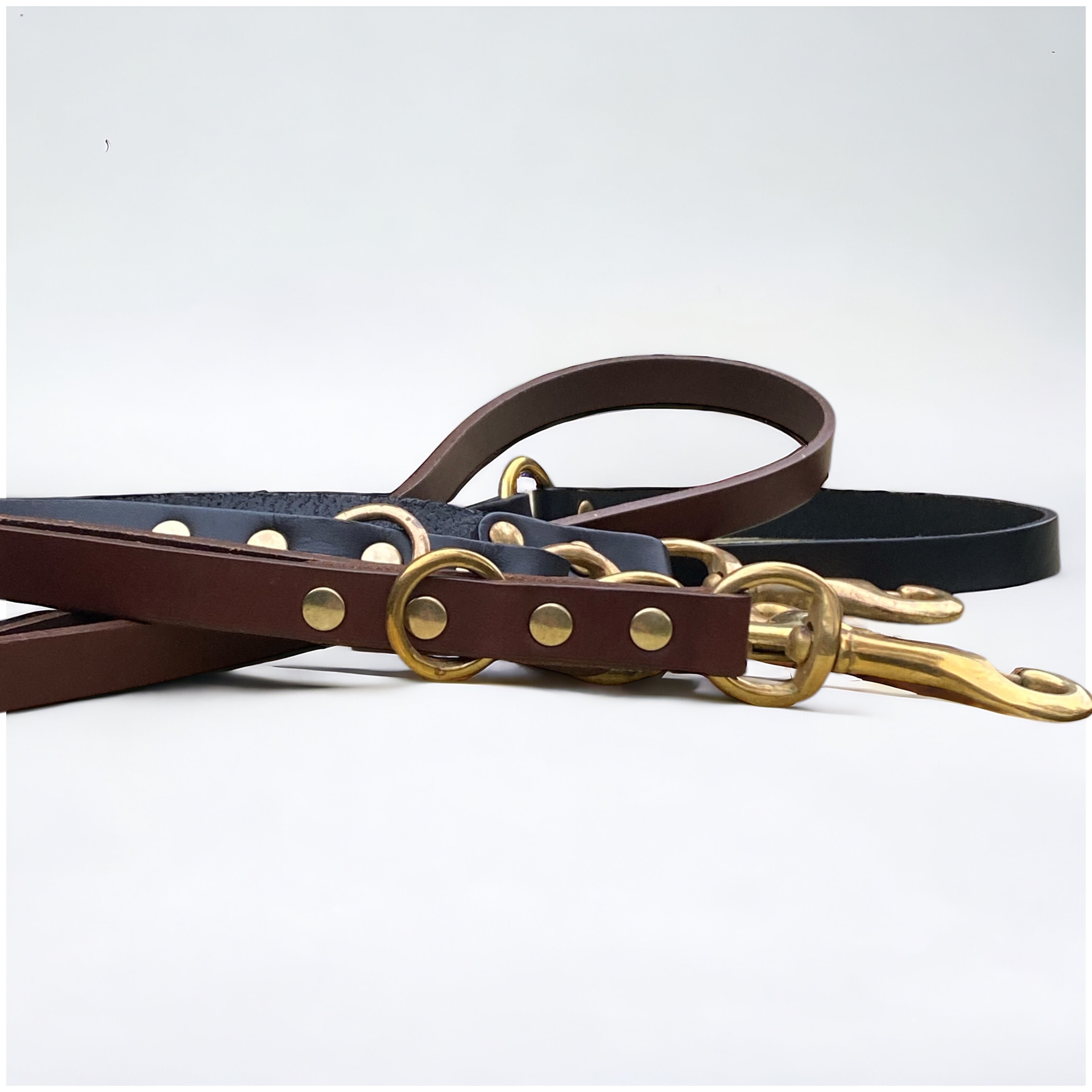 Side-by-side close-up of chestnut brown and black handmade luxury leather hands free dog leads with solid brass hardware.