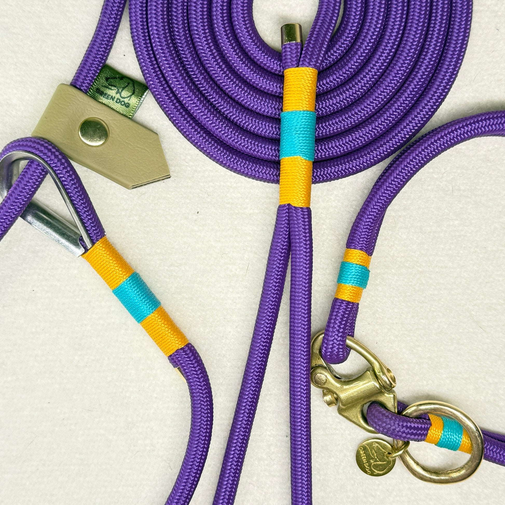 Close up of the deep purple 6mm rope lead and Greenwich Yarn Mini dog collar showing airforce gold and teal nano binding, brass Swedish sailing shackle, and small brass o-ring detail.