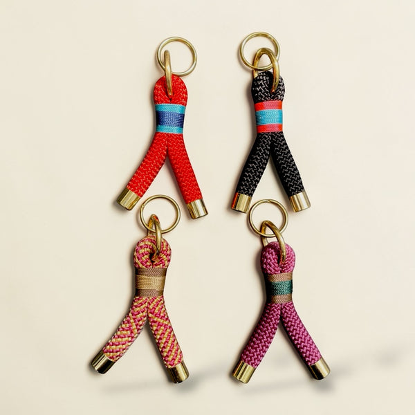 Four customisable Greenwich Yarn rope keyrings with premium brass hardware, shown in red, black, crown coronaion and maroon colour-ways on a neutral background.
