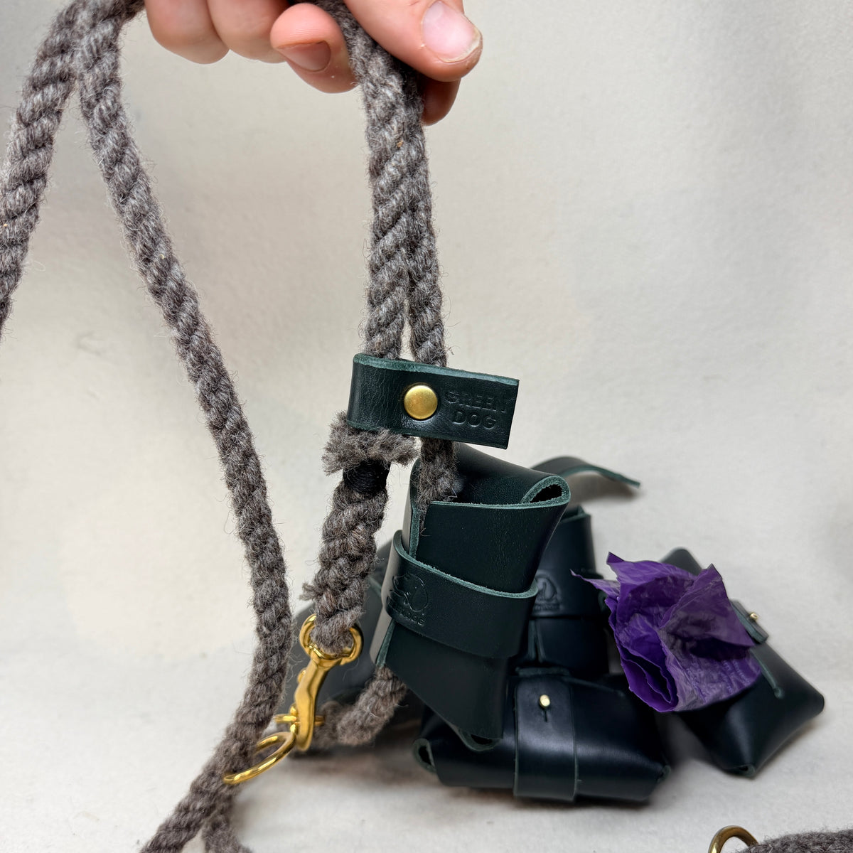 Hunter green leather poo bag holder open to show a roll of poo bags stored inside, with its stud fastened leather tab closure in the Sam Browne style