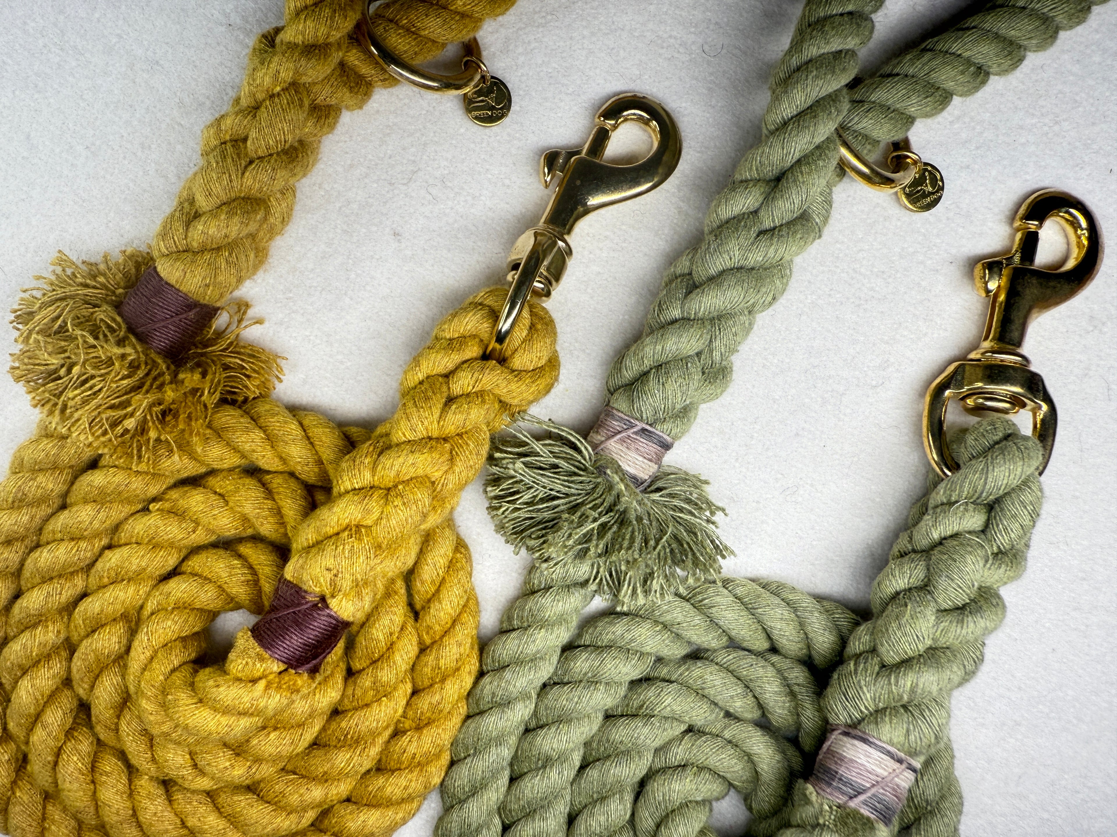 A close up of the Mustard Yellow and Olive Green Cotton braided rope dog leashes with brass hardware on a light woollen background
