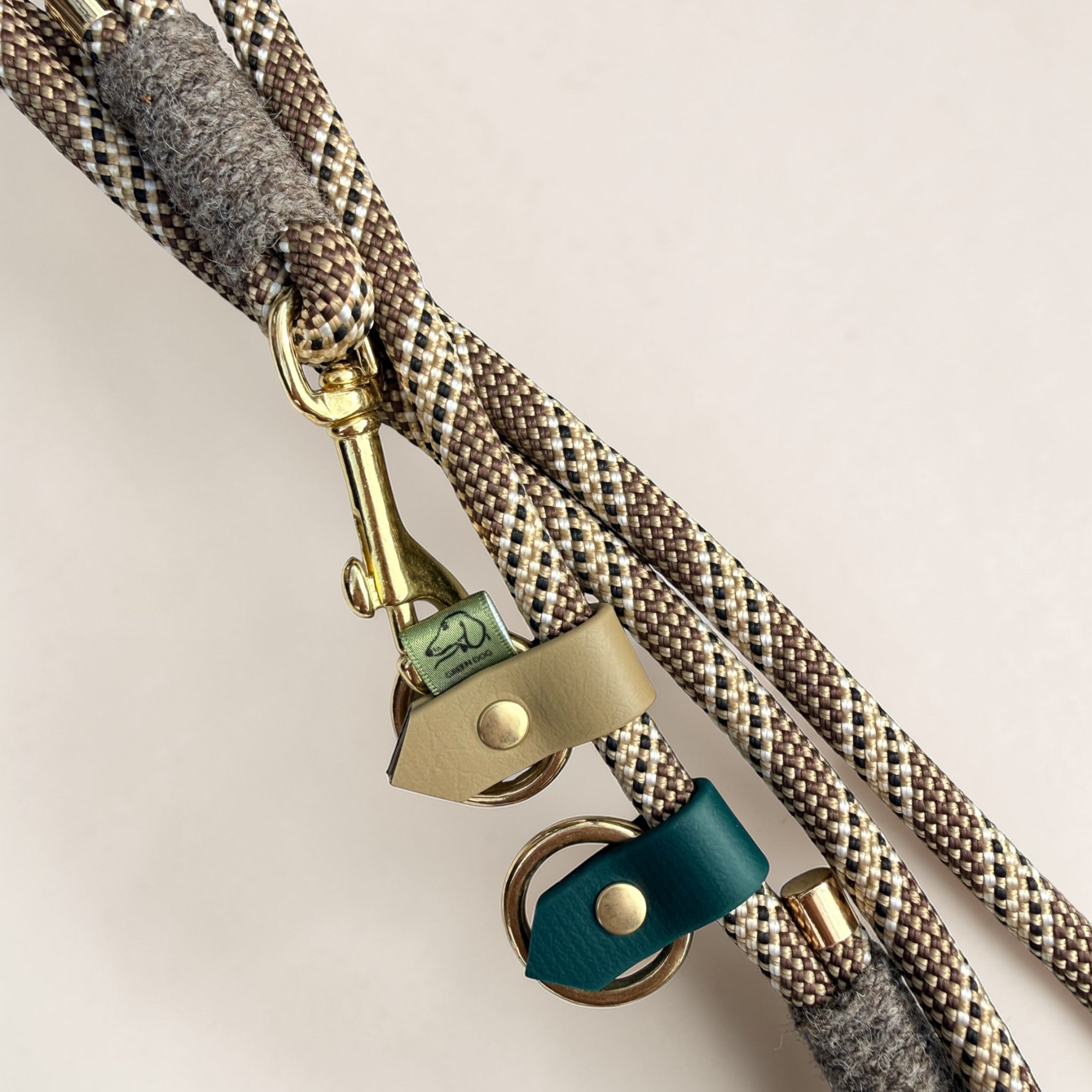 Close-up of Brampton Hybrid rope lead hardware — solid brass snap clip, beige BioThane stopper, teal BioThane loop tab, Brampton wool binding and Green Dog woven label