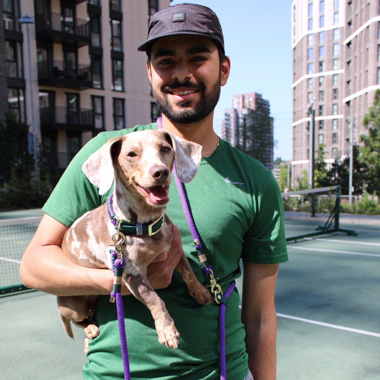 Bruno the Dachshund wearing the Centre Court Fishtail dog collar, standing beside his dad on the tennis court, who’s sporting the 8ft hands-free rope lead in Wimbledon-inspired colours.