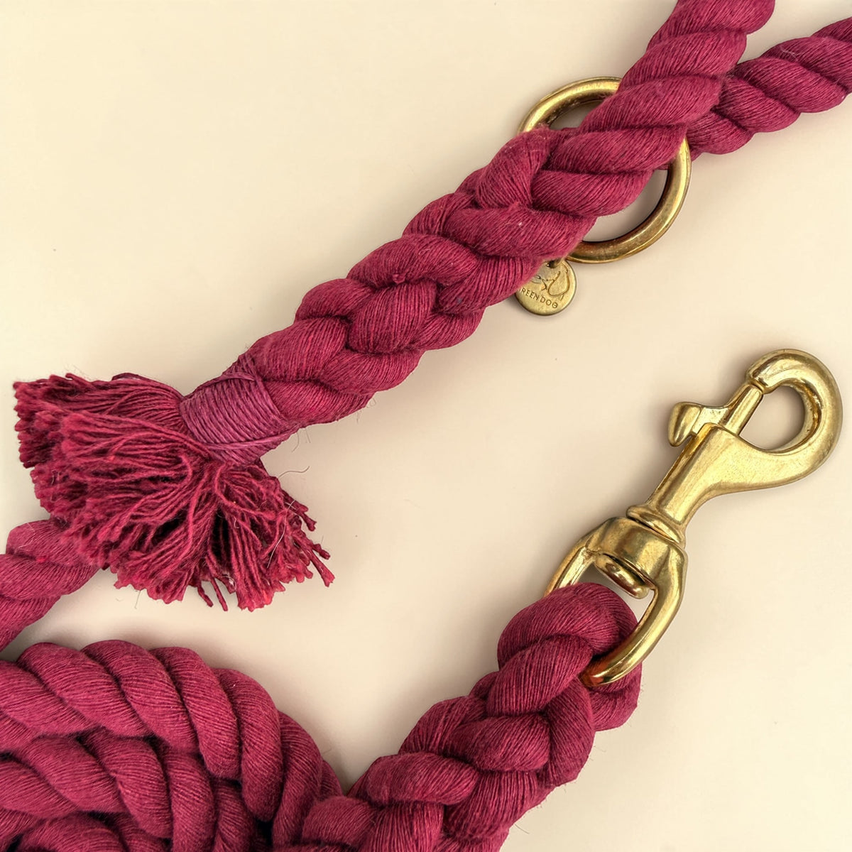 Close-up of the solid brass trigger snap clip and O-ring on a burgundy handmade cotton rope dog lead, with the Green Dog brass disc and the handle tassel