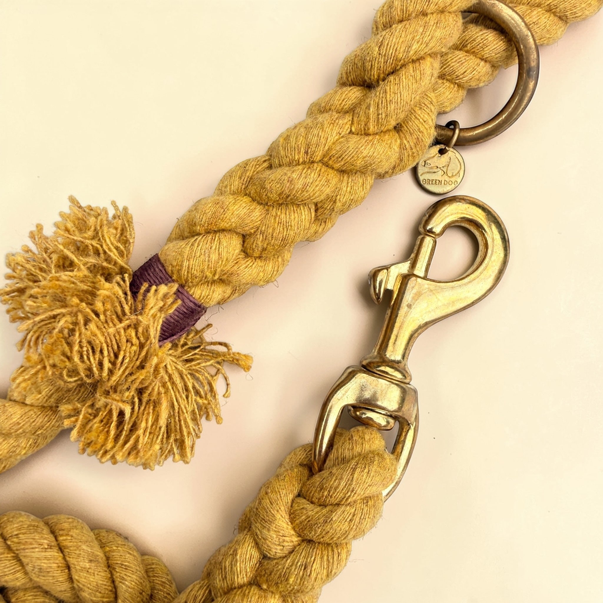 Close-up of the solid brass trigger snap clip and O-ring on a harvest yellow handmade cotton rope dog lead, with the Green Dog brass disc and the handle tassel