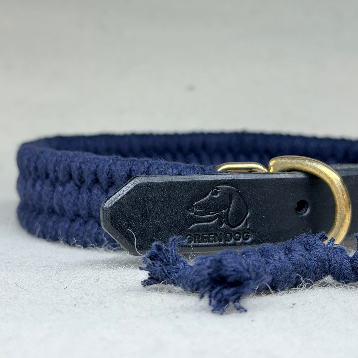 Close-up of midnight blue woven cotton dog collar showing embossed Green Dog leather patch, solid brass D-ring and matching cotton bone charm