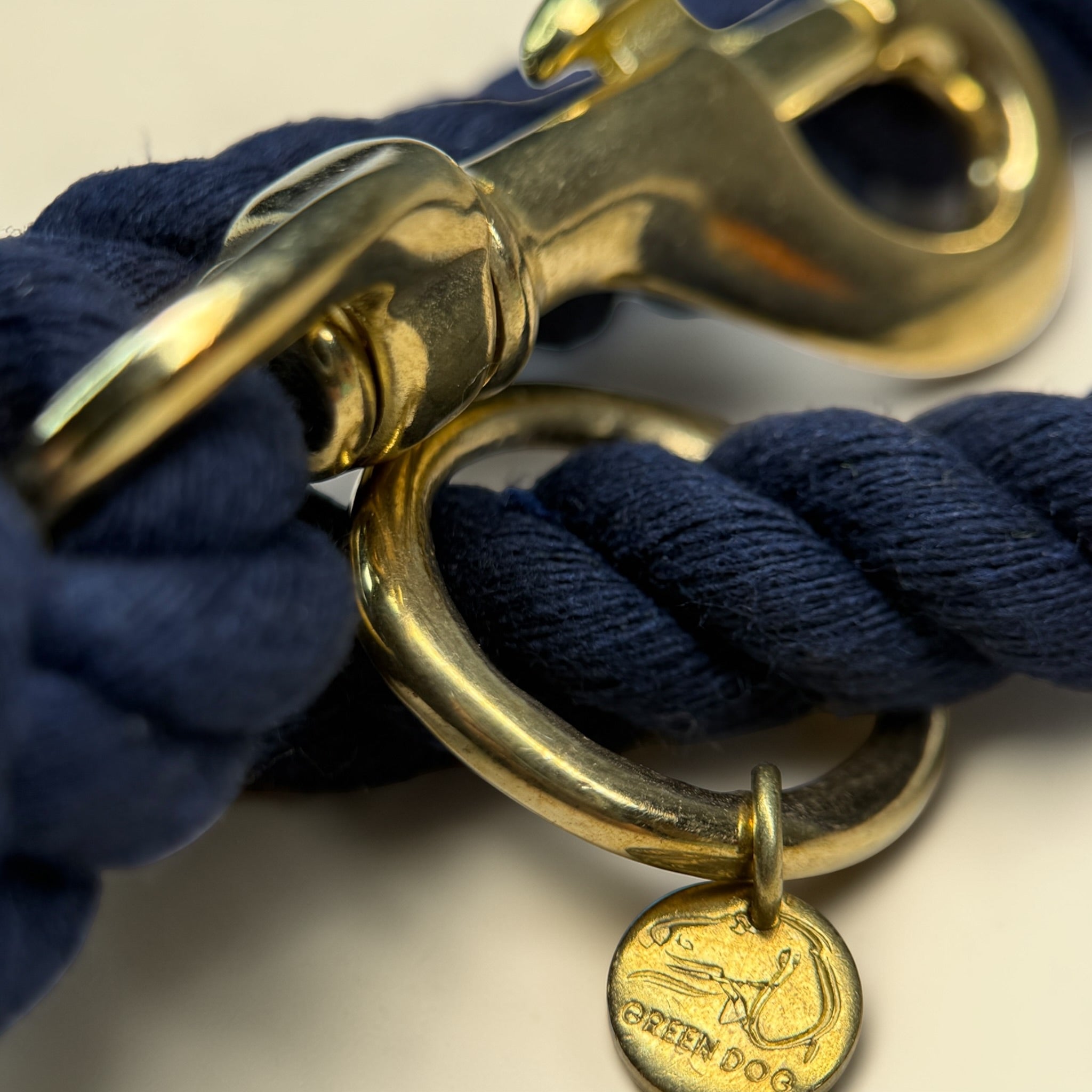 Close-up of the solid brass trigger snap clip and O-ring on a midnight blue handmade cotton rope dog lead, with the Green Dog brass disc stamped with the logo
