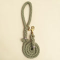 Olive green handmade cotton rope dog lead coiled flat lay, with solid brass snap clip, brass O-ring, Green Dog charm tag and lilac binding detail