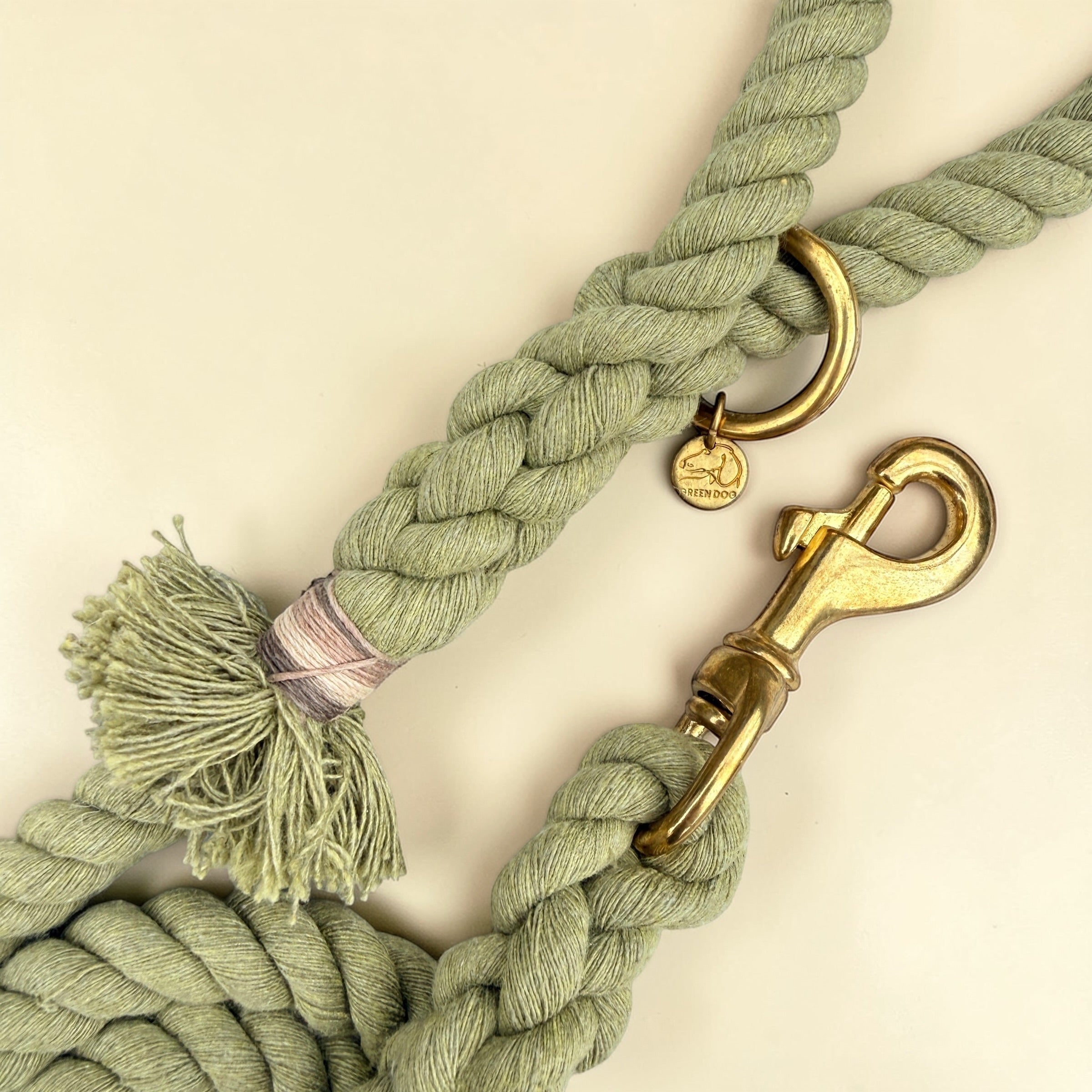 Close-up of the solid brass trigger snap clip and O-ring on an olive green handmade cotton rope dog lead, with the Green Dog brass disc and the signature handle tassel