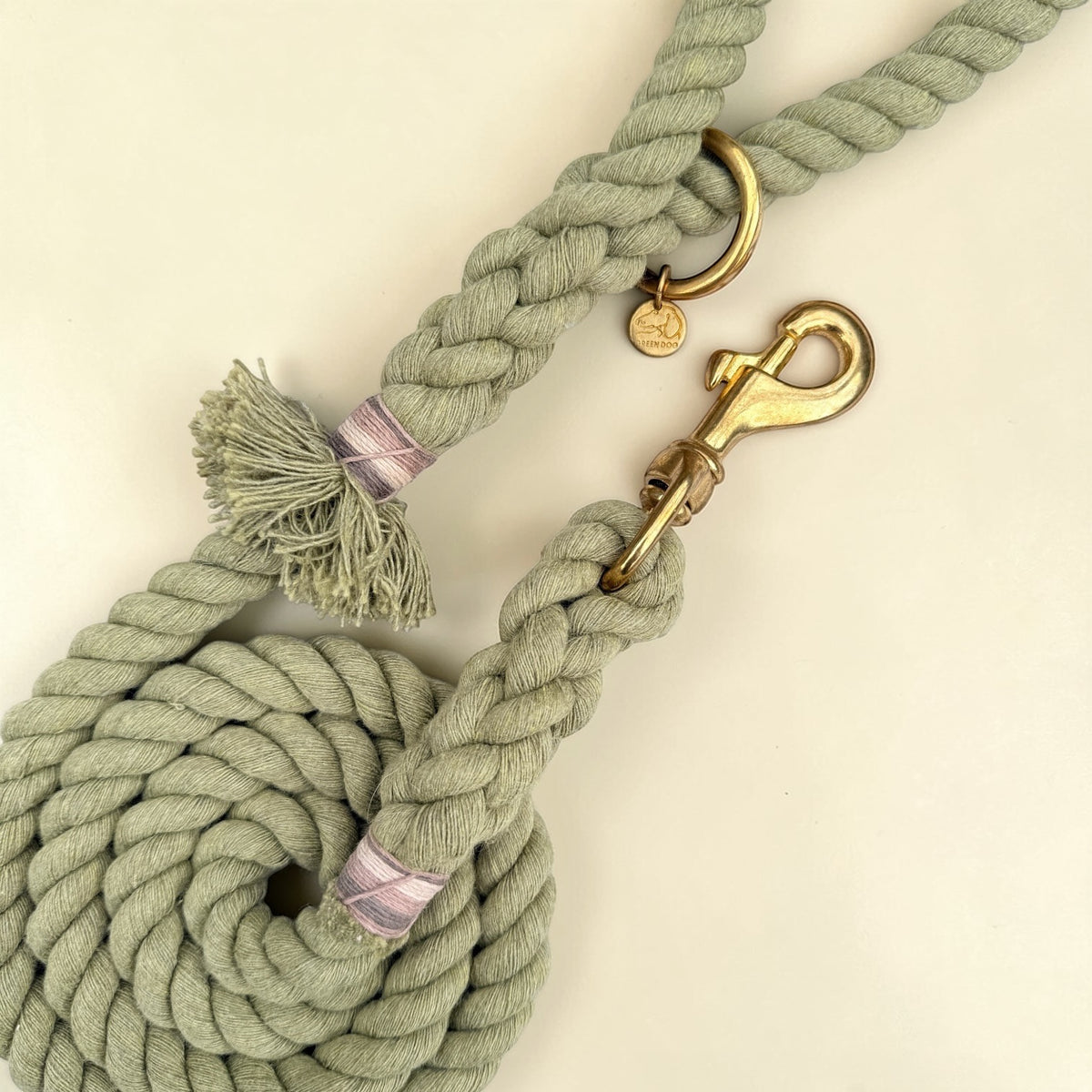 Close-up of olive green cotton rope dog lead showing the frayed tassel at the handle, mixed striped binding, brass O-ring and solid brass trigger snap clip